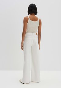White wide-leg trousers with a high waist, featuring back pockets and a small tan label on the waistband. Paired with a light beige tank top.