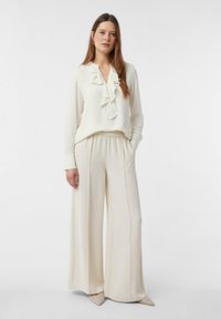 Kremowa bluzka z falbaniastym dekoltem, długimi rękawami oraz dopasowanymi spodniami o wysokim stanie i szerokich nogawkach. Teksturowany materiał i gładkie wykończenie w całej powierzchni.