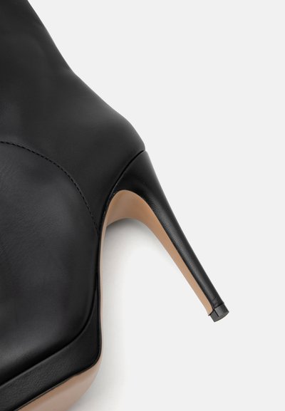 Chaussure à talon haut en cuir noir avec bout pointu et talon aiguille fin sur un fond neutre.