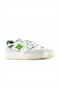 White sneakers with green accents, featuring leather and suede materials. Design includes perforated sections, a logo, and a textured rubber sole.