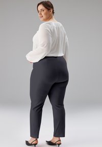 Weiße Langarmbluse mit plissiertem Rücken, kombiniert mit enganliegenden marineblauen Hosen und schwarzen Sandaletten mit Absatz. Glatte Texturen, maßgeschneidertes Design.