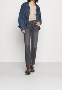 Veste en denim bleu foncé, pull en maille texturée beige, jean droit noir et bottines marron brillantes à lacets.