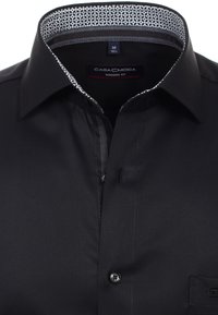 Zwarte shirt met een moderne pasvorm, voorzien van een gemêleerde witte en grijze kraag, knoopsluiting en een gladde stoftextuur. Detail van een borstzakje.