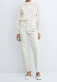 Light beige knitted sweater with a textured pattern, paired with high-waisted, straight-leg ivory jeans. Footwear is flat, white shoes.