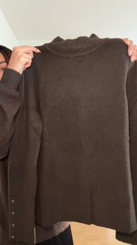 Brown knitted sweater with a high neckline, long sleeves, and button detailing along one side. Texture appears soft and smooth.