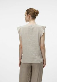 Ljust beige topp med volangärmar, strukturerad tyg och avslappnad passform. Bärs med lösa, krämfärgade byxor. Minimalistisk design.