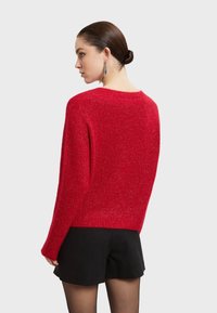 Roter, strukturierter Pullover mit lässiger Passform und weiten Ärmeln. Besitzt einen Rundhalsausschnitt und dezente Glitzereffekte für zusätzliche Details.