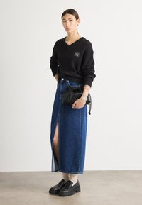 Črna pletena jopica z V-izrezom. Dolga modra jeans krila z odprtino spredaj. Črna torbica s vrvico. Debeli črni platform čevlji.