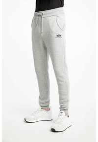 Pantalon de survêtement gris en tissu doux et texturé, avec une taille à cordon et des poches latérales, portant un logo imprimé sur la jambe gauche.