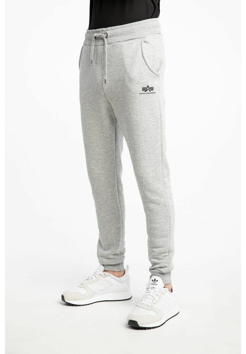 Pantalon de survêtement gris en tissu doux et texturé, avec une taille à cordon et des poches latérales, portant un logo imprimé sur la jambe gauche.