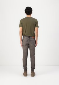 Dark gray jeans with straight cut, slim fit, and back pockets. Olive green t-shirt, short sleeves, round neck. Beige boots with textured sole.