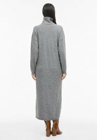 Abito grigio a maniche lunghe e collo alto in morbido tessuto a maglia, con una vestibilità comoda e spacchi laterali, abbinato a stivali marroni con tacco.