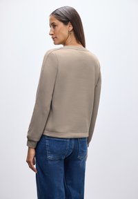 Felpa beige realizzata in tessuto morbido, con colletto a girocollo, maniche lunghe e polsini a coste, abbinata a jeans in denim blu.