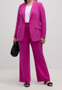 Fuchsia skräddarsydd kavaj och vida byxor kombinerat med en vit topp. Outfiten har en slät struktur och en minimalistisk design.