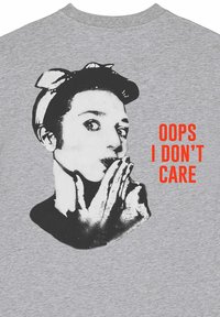 T-shirt en coton gris présentant un graphique noir et blanc d'une personne avec un bandeau et du texte rouge disant "OUPS, JE M'EN FOUS."