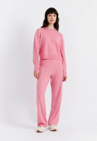 Cardigan rosa a maglia con scollo rotondo e bottoni, abbinato a pantaloni rosa coordinati con vestibilità rilassata e dettagli nelle cuciture laterali.