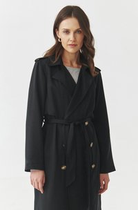 Black trench coat with a belted waist, double-breasted buttons, and a wide collar, made of smooth fabric. Accents include shoulder epaulets.