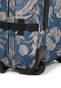 Rullaava matkalaukku, jossa on laivastonsininen kangas ja beige trooppinen lehtikuvio, mustat metalliosat, vahvistetut kulmat ja kaksipyöräinen alusta.