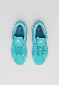 Turkosa sportskor med meshuppbyggnad, vadderad krage och snörning. Har vit logotyp och texturerade detaljer på sidorna.