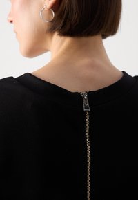Vêtement noir avec un col montant et une fermeture éclair métallique visible à l'arrière, présentant une texture lisse et une coupe ajustée.