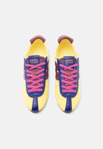 Κίτρινα, μπλε και μπορντό sneakers Marc Jacobs με ροζ κορδόνια, φωτογραφημένα από πάνω σε ανοιχτό φόντο.