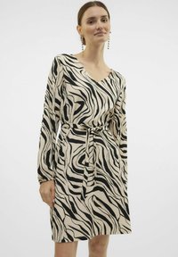 Langärmelig jurkje met een v-hals en een ceintuur in de taille, gemaakt van gestructureerde stof in een beige en zwart zebra patroon.