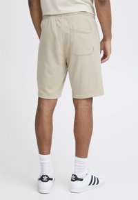 Pantalones cortos de algodón beige con una cinturilla elástica, que cuentan con un único bolsillo trasero y un corte relajado, combinados con zapatillas blancas y calcetines.