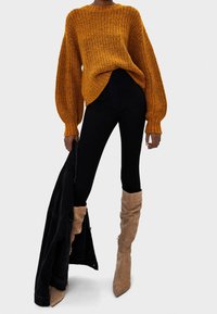 Grob gestrickter Pullover in Senfgelb, legerer Schnitt mit Ballonärmeln. Kombiniert mit schwarzen Skinny Jeans und taupefarbenen Over-the-Knee-Stiefeln mit Absatz.