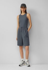 Canotta grigia a costine e pantaloni corti grigi con coulisse abbinati. Modello che indossa un cappellino grigio e scarpe da ginnastica argento sportive con calzini bianchi.