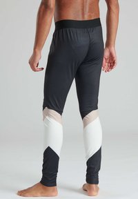 Schwarze Sportleggings mit einem breiten schwarzen Taillenbund, versehen mit weißen und beigen Zickzackmustern an den Unterschenkeln. Weicher, glatter Stoff.