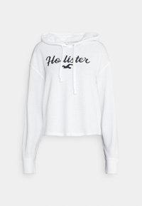 Sweat à capuche court blanc en tissu texturé, doté d'une capuche à cordon de serrage et du logo « Hollister » brodé en bleu marine sur le devant.