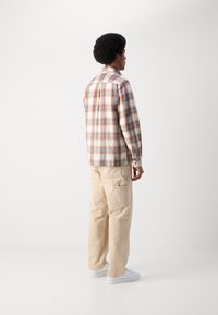 Checkered flannel shirt in brown, white, and blue; beige cargo pants; model standing with back turned; white sneakers.