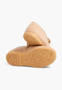Zapatos de ante marrón claro con un diseño redondeado, suela de goma texturizada que presenta patrones florales y de corazones. Cierre de velcro en el lateral.