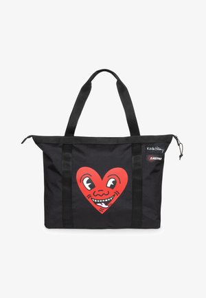 Borsa a tracolla nera con una grande grafica a forma di cuore rosso con un volto sorridente. Realizzata in tessuto resistente, presenta due manici robusti e una chiusura con zip.