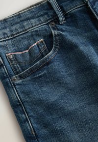 Jeans de mezclilla azul oscuro con un diseño clásico. Las características incluyen un diseño de cinco bolsillos, costura visible y un pequeño bolsillo trasero.