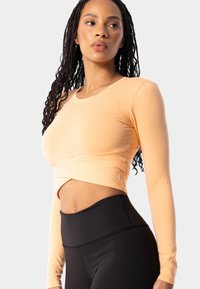 Garās piedurknes persiku krūšturis ar savīti priekšu, savienots ar augsto vidukļa melno legingu. Gluda tekstūra, pieguļošs siluets.