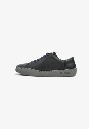 Baskets en cuir noir avec une texture lisse, semelle en caoutchouc grise, lacets bleu marine et branding subtil au niveau du talon. Design à bout rond.