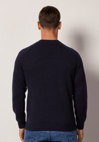 Mörkblått stickat tröja med rund halsringning, långa ärmar, ribbade manschetter och en texturerad yta. Har en figurnära midja.