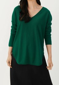 Vihreä, pitkähihaista V-kaula-aukkoista neulepaitaa, jossa on rento istuvuus, pyöreä helma ja ribbireunat. Pehmeä materiaali, jossa on sileä pinta.