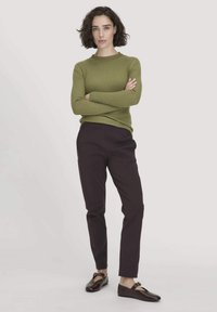 Olivgrüner, gerippter Strickpullover kombiniert mit dunkelvioletten, geraden Hosen und braunen flachen Schuhen mit einer Schnallendetail.