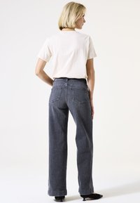 Hoch-taillierte graue Jeans mit einem geraden Bein, fünf Taschen und sichtbaren Nähten, kombiniert mit einem weißen T-Shirt mit kurzen Ärmeln.