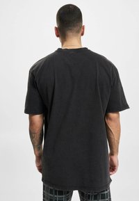 Svart, oversized t-skjorte med korte ermer og rund hals. Laget av bomull, med en lett slitt tekstur og sydd detaljer ved sømmene.