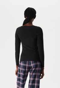 Black long-sleeve top with a wide neckline, paired with plaid trousers in navy, purple, and gray. Smooth fabric with a fitted silhouette.
