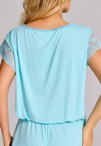 Jasnoniebieski bluzka z krótkim rękawem z koronkowymi wykończeniami rękawów i dekoltu, wykonana z miękkiego materiału o luźnym kroju.