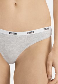 Culotte en coton gris avec une ceinture élastique blanche ornée du logo "PUMA" en noir. Texture lisse, design taille basse.