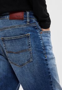 Τζιν τζιν με μπλε πλύση, δερμάτινο ταμπελάκι με το λογότυπο "Pepe Jeans" και πορτοκαλί ραφές. Διαθέτει πίσω τσέπες με μοναδικό σχέδιο ραφής.