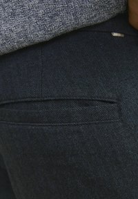 Mörk marinblå byxor med ett subtilt herringbone-mönster, med en standard bakficka och synliga sömmar.