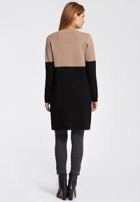 Robe en laine jusqu'au genou, composée d'une partie supérieure beige et d'une partie inférieure noire unie, fabriquée dans un matériau doux et dotée de longues manches.