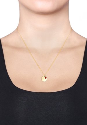 Collier en or avec un pendentif rond, présentant une petite pierre d'accent rouge. La chaîne est fine et délicate, complétant le design du pendentif.