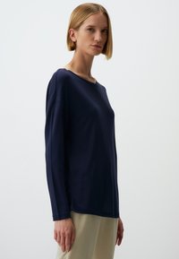 Navy Langarmoberteil mit weitem Ausschnitt und lässiger Passform. Weiche Textur mit glatter Oberfläche. Kombiniert mit hellen Hosen.